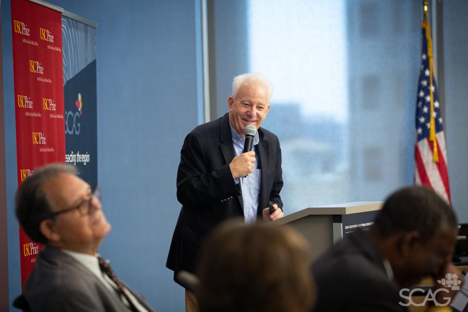 Keynote speaker Bill Fulton stands at a podium to  address the attendees at the 2024 Southern California Demographic Workshop.