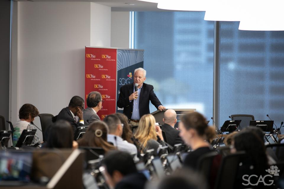 Keynote speaker Bill Fulton stands at a podium to  address the attendees at the 2024 Southern California Demographic Workshop.